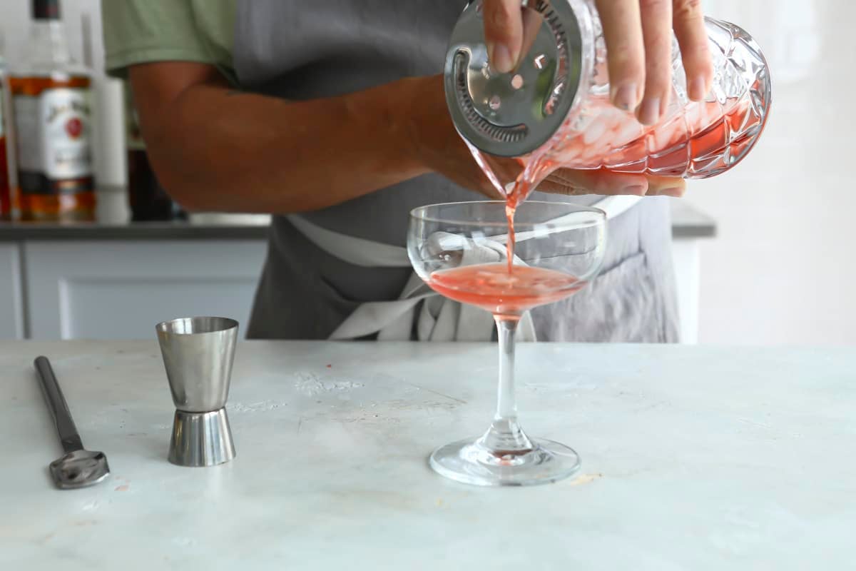 A Boulevardier Cocktail being strained into a coupe glass.