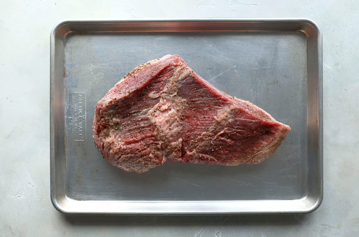 A beef brisket on a baking sheet before being cooked.