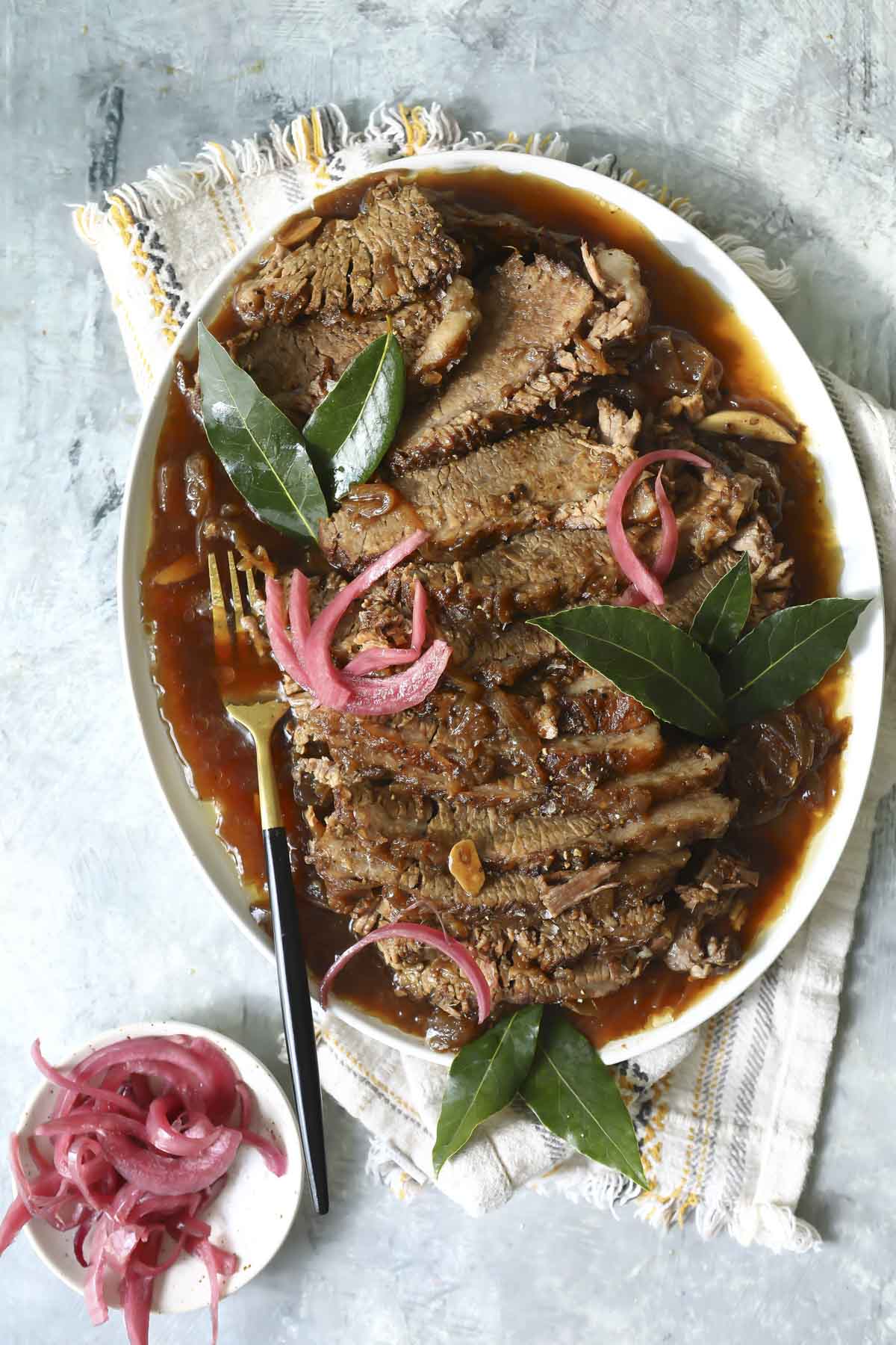 Braised beef brisket slices on a plate with red onions.