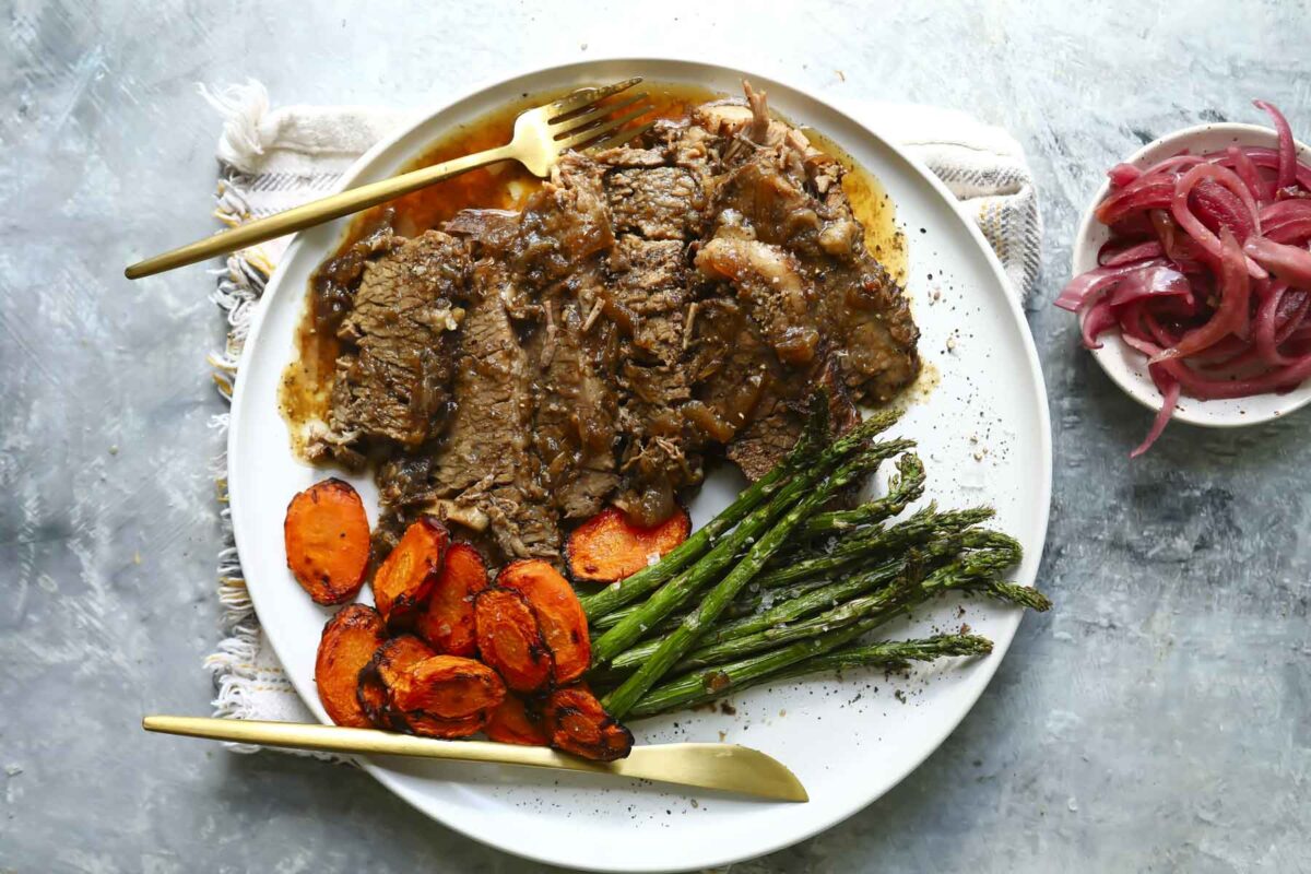 Braised beef brisket slices on a plate with carrots and asparagus.