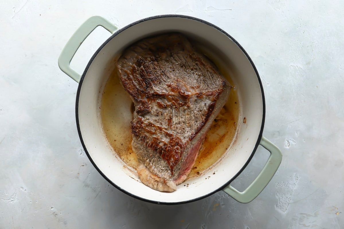 A beef brisket being browned in a Dutch oven.