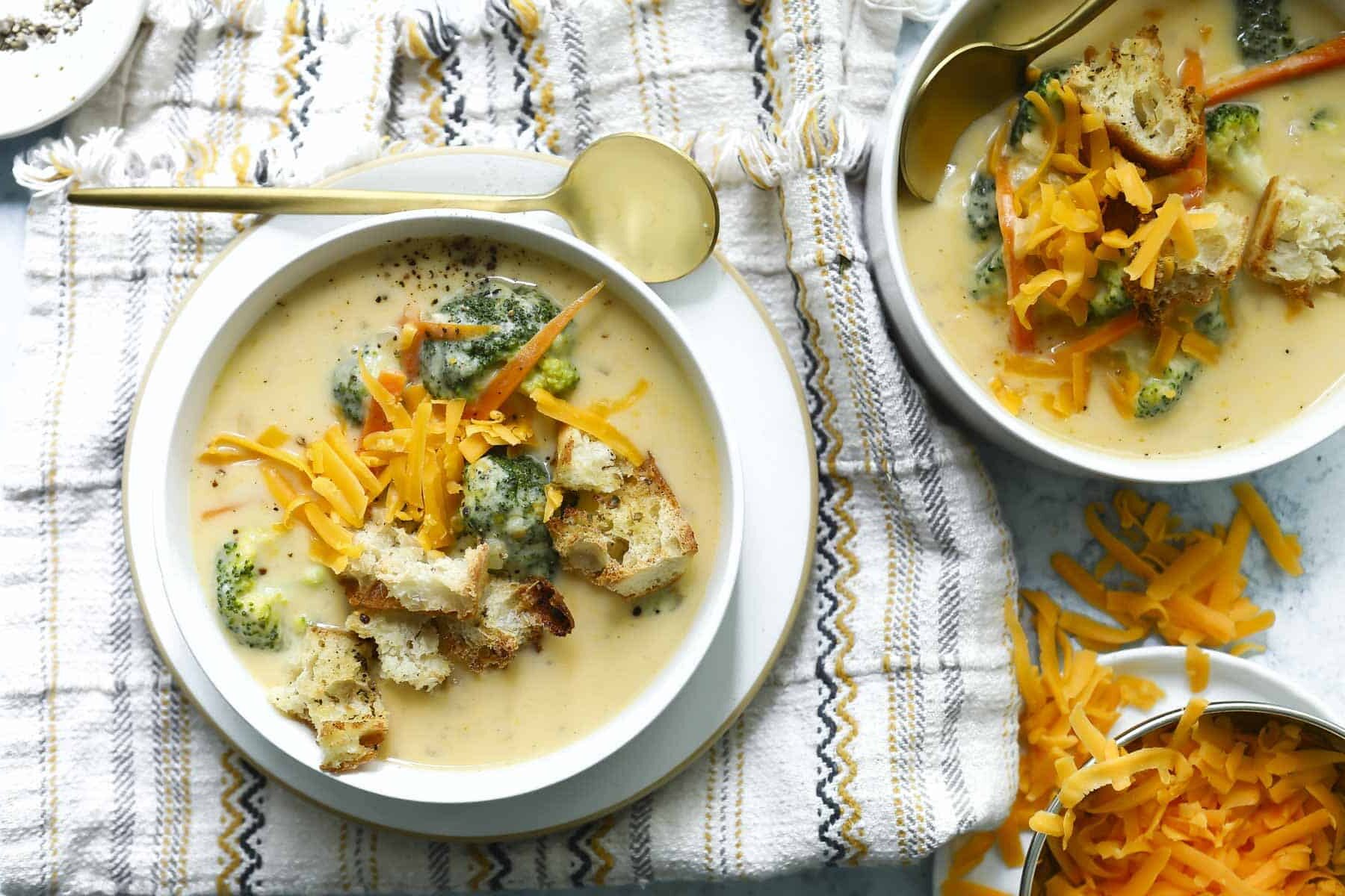 Two bowls of broccoli cheese soup garnished with croutons and cheese.