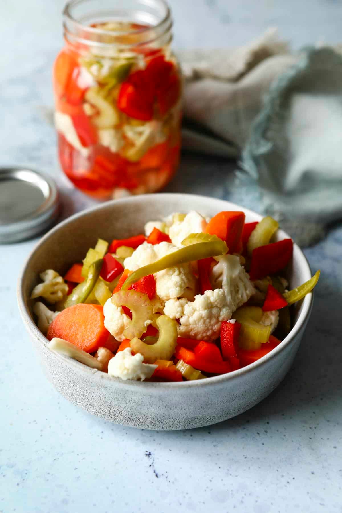 A bowl of Giardiniera next to a mason jar of Giardiniera.