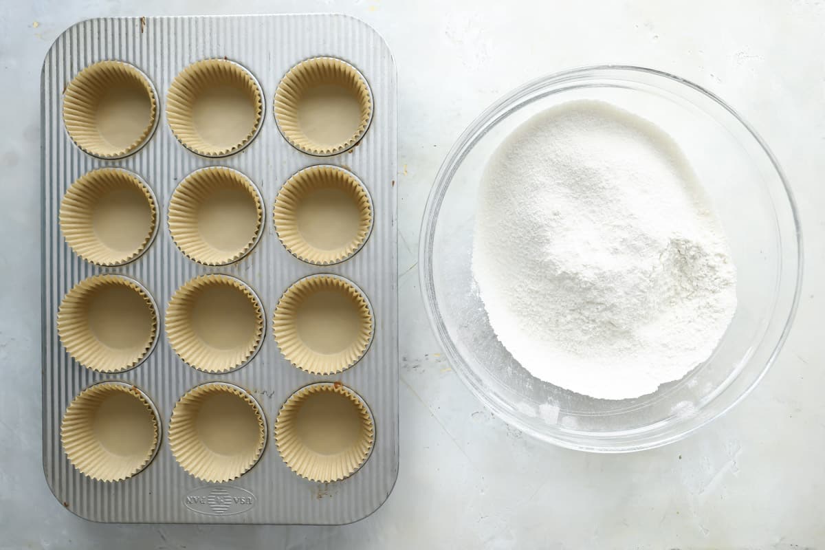 Dry ingredients for gluten-free muffins in a mixing bowl next to a muffin tin.