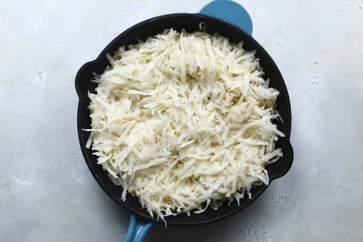 Raw hash browns in a skillet.