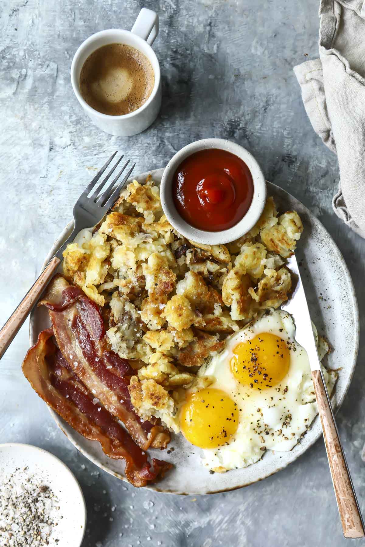 A plate of sunny-side up eggs, hashbrowns, bacon and ketchup.