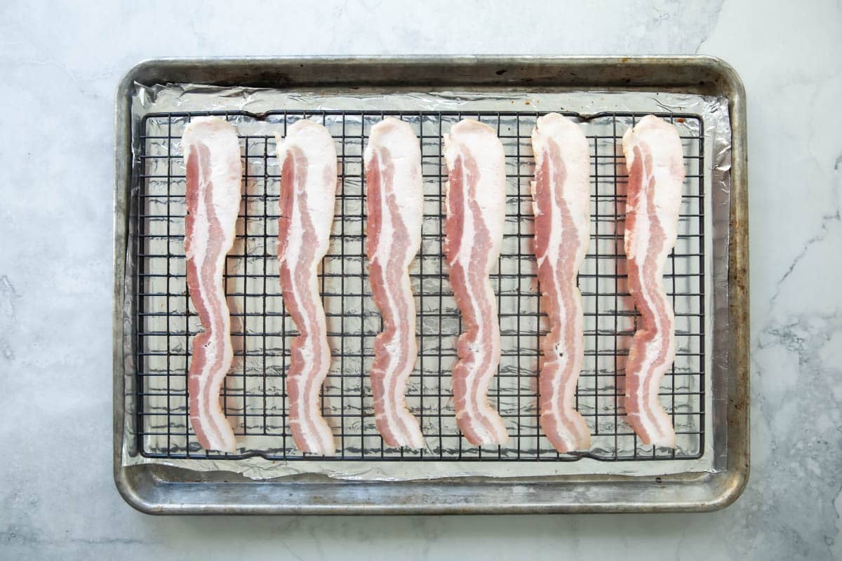 Raw bacon on a rack set over a foil-lined baking sheet.