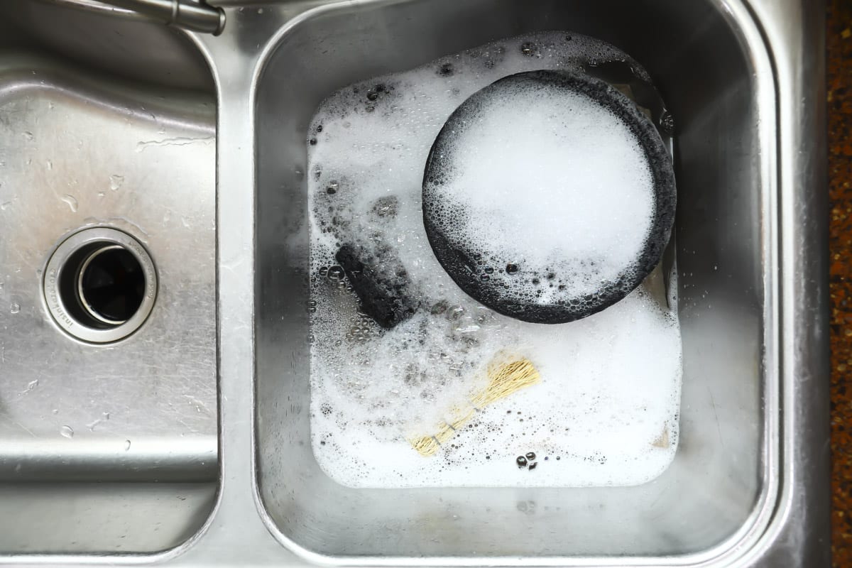 A molcajete and root brush in a sink with soap.