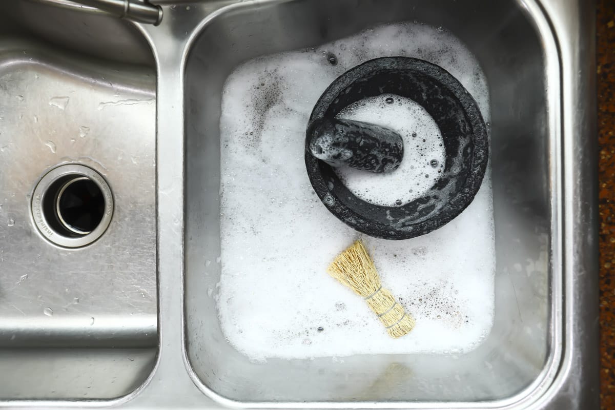 A molcajete and root brush in a sink with soap.