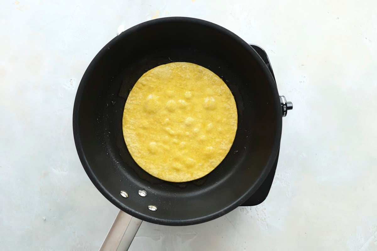 A corn tortilla being warmed in a black skillet.