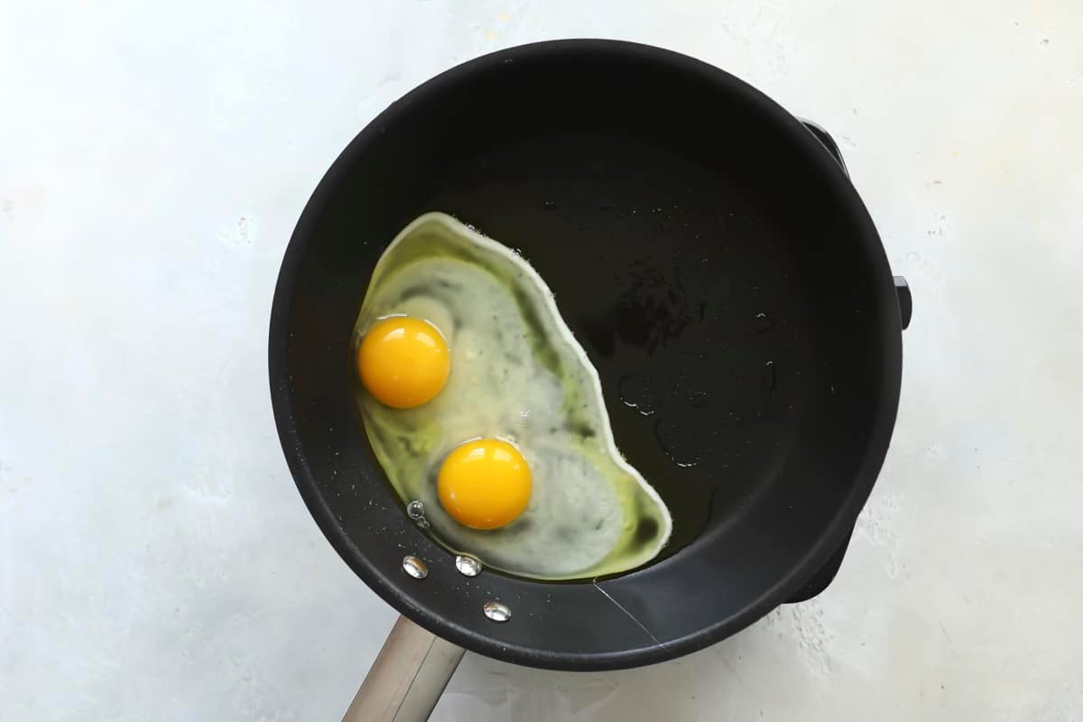 Two cracked eggs cooking in a black skillet.