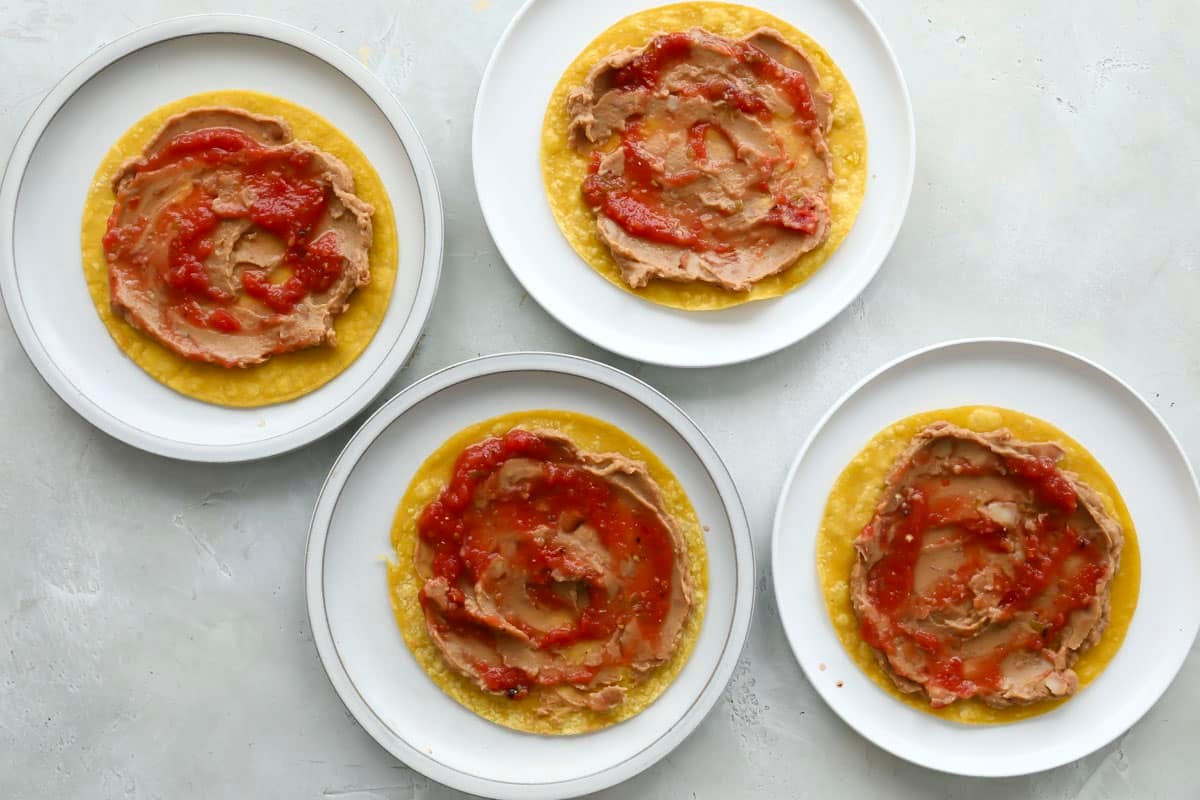 Flour plates with tortillas topped with refried beans and salsa ranchera.