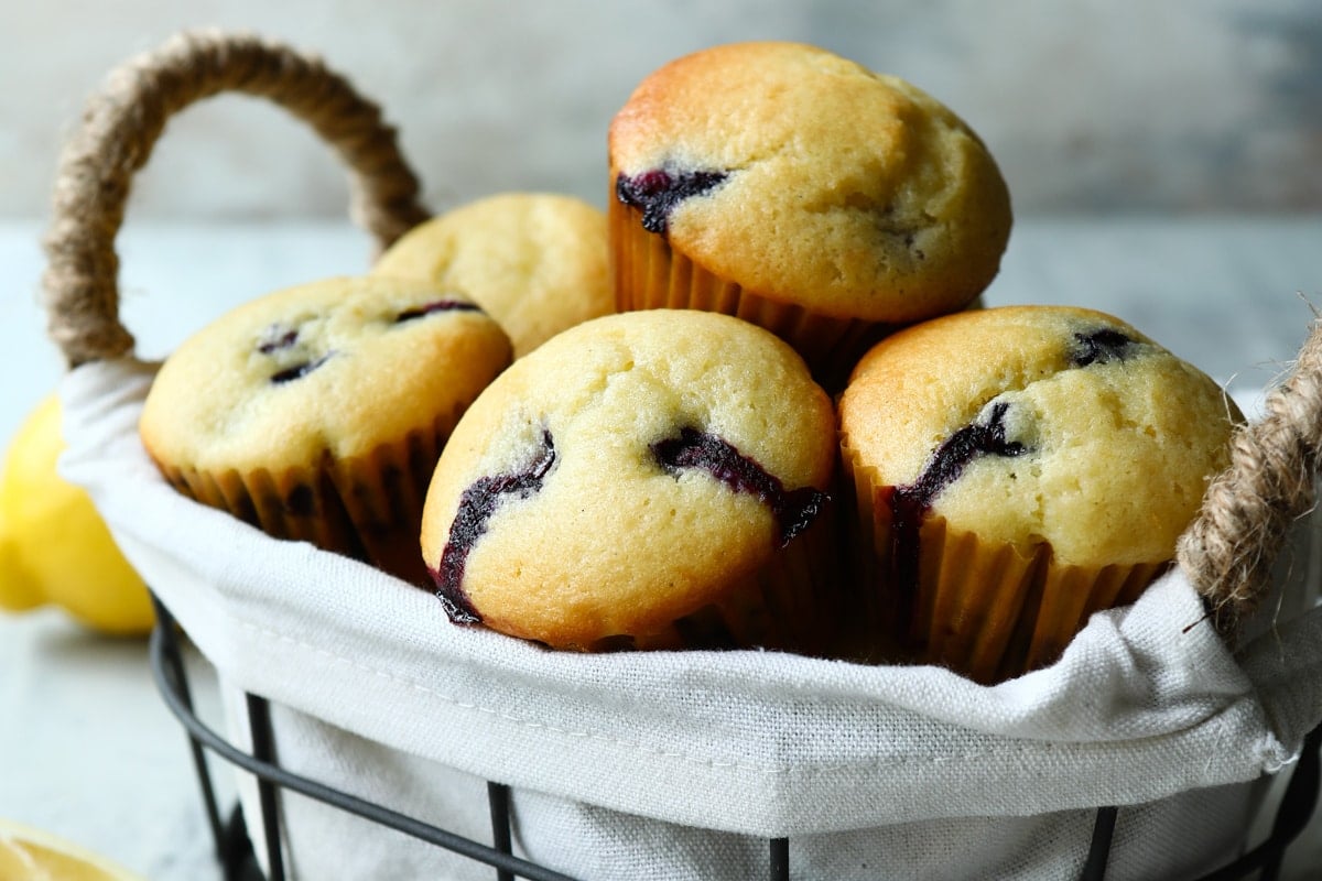 Lemon blueberry muffins in a basket with a bowl of blueberries.