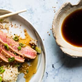 Ahi tuna on a small gray plate with rice and chopsticks.