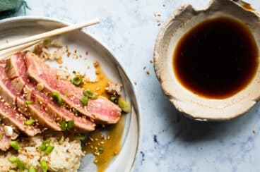 Ahi tuna on a small gray plate with rice and chopsticks.