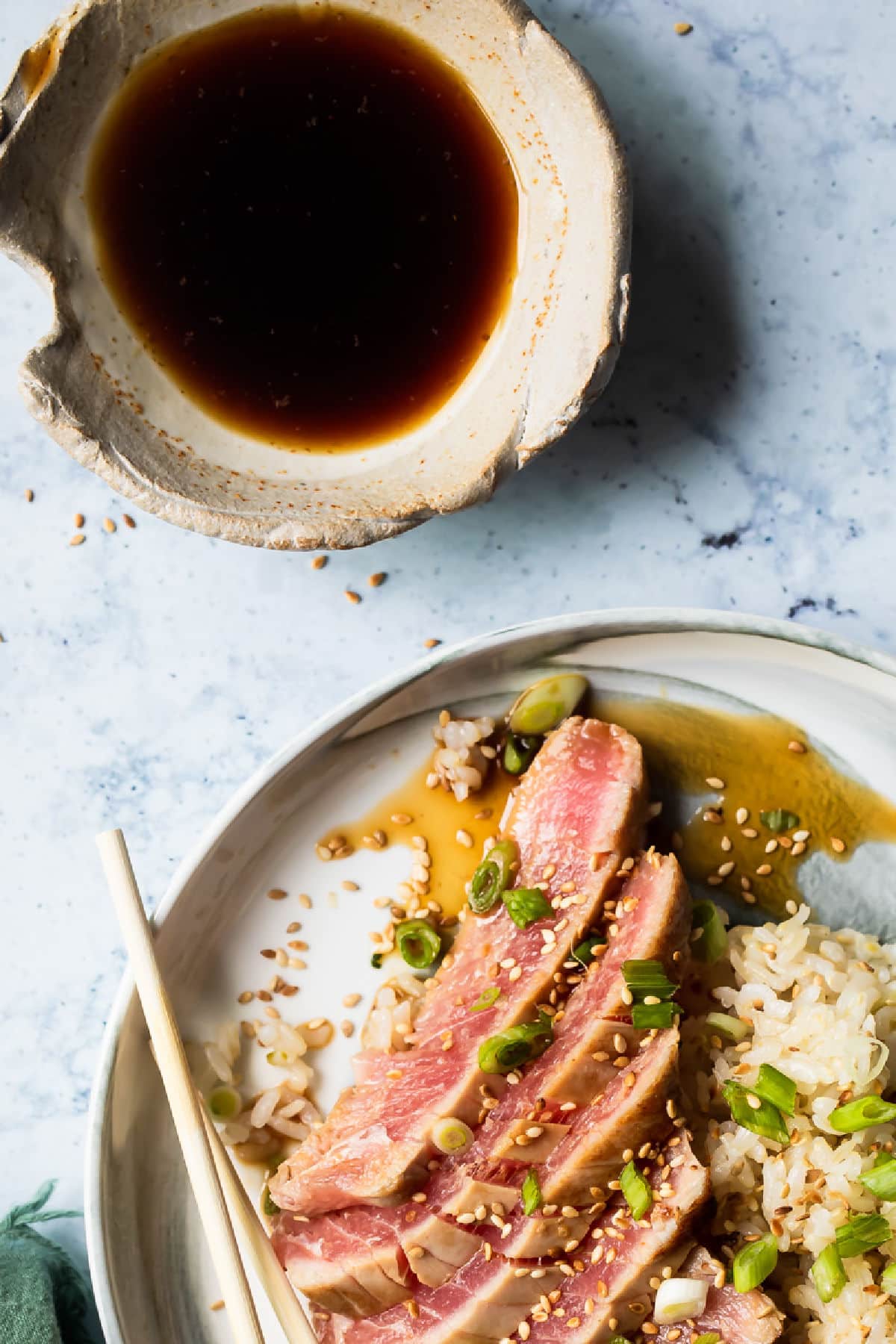 Ahi tuna on a small gray plate with rice and chopsticks.