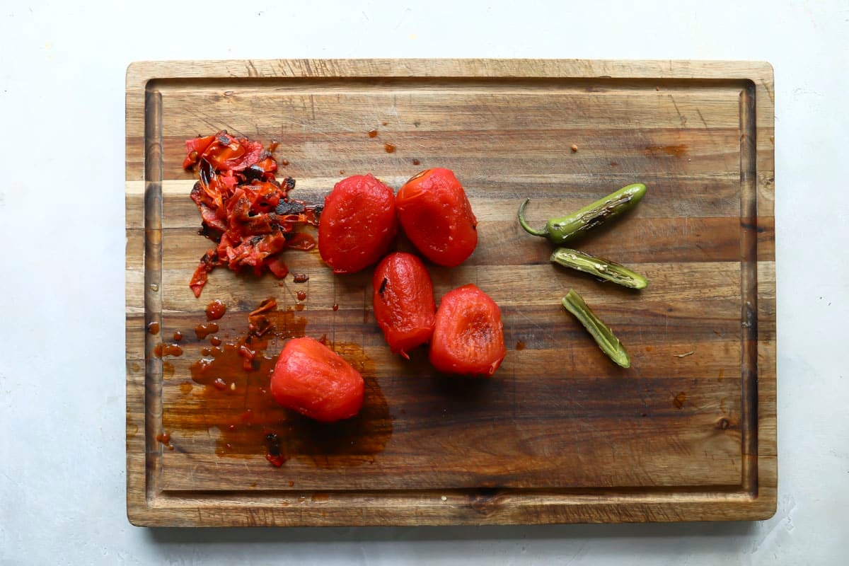 Roasted and peeled roma tomatoes and chiles on a wooden cutting board.