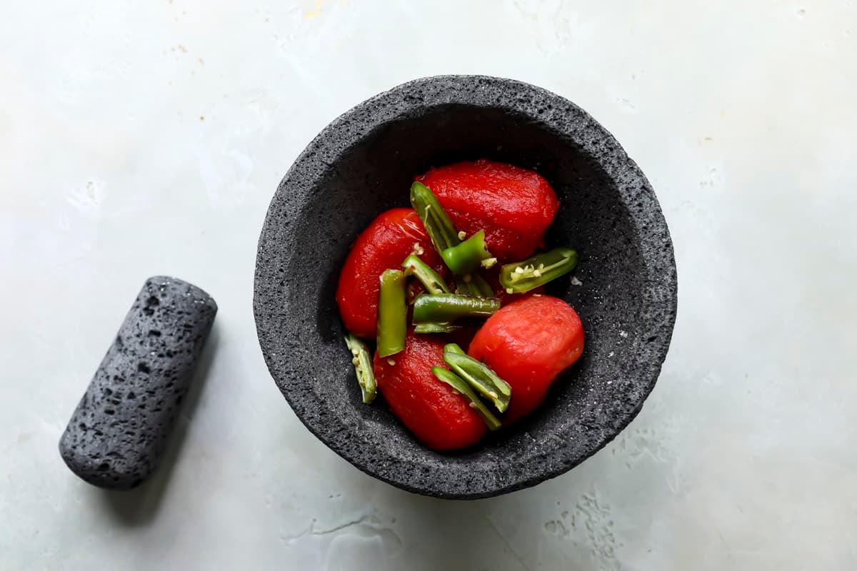 Peeled roma tomatoes and serrano chilies in a molcajete.
