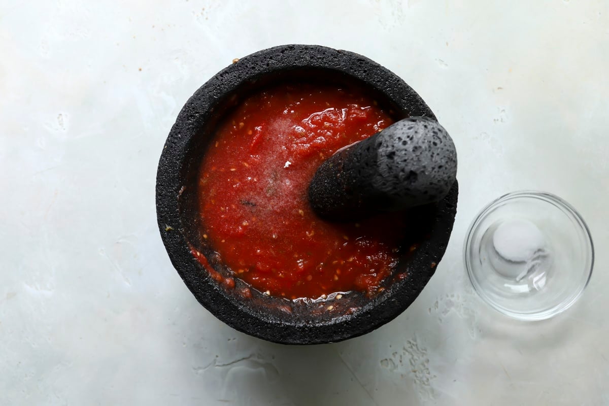 A molcajete of salsa ranchera next to a small bowl of salt.
