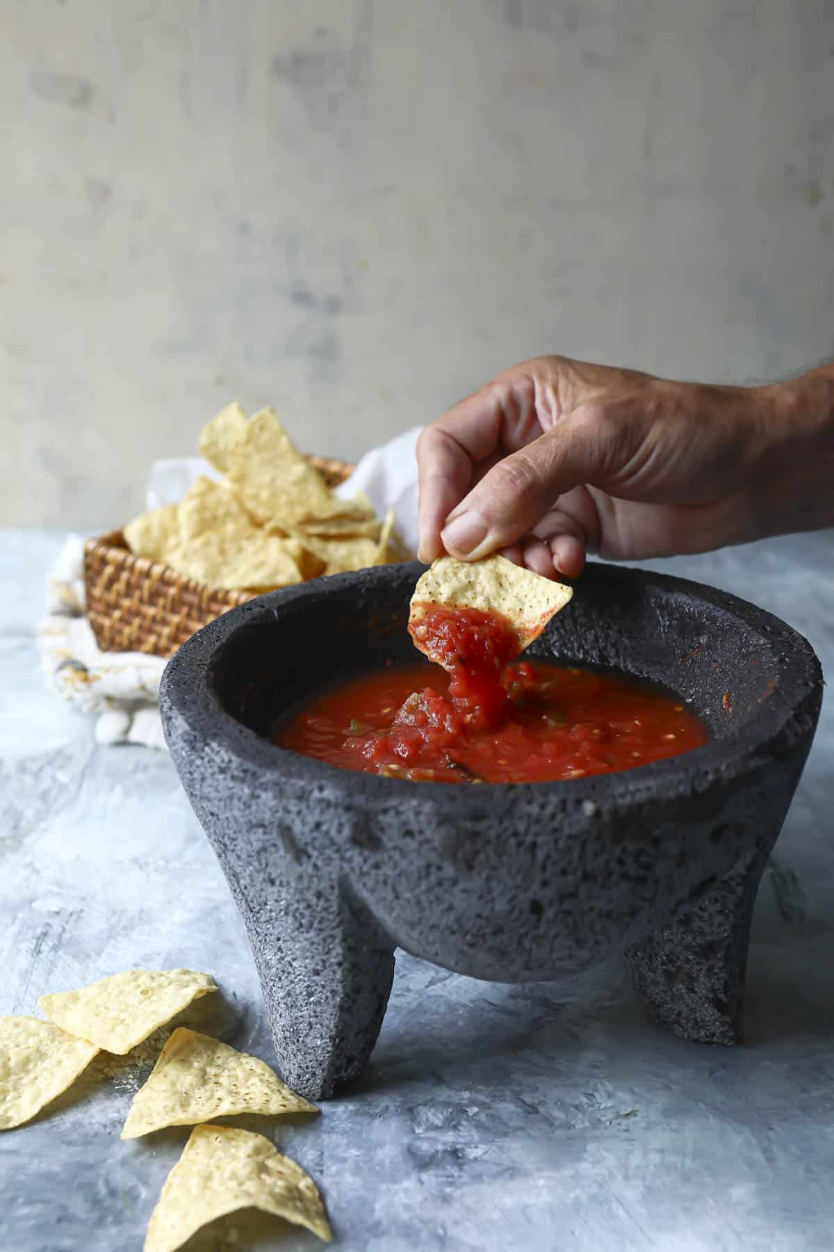 Someone dipping a tortilla chip in a molcajete of salsa ranchera.