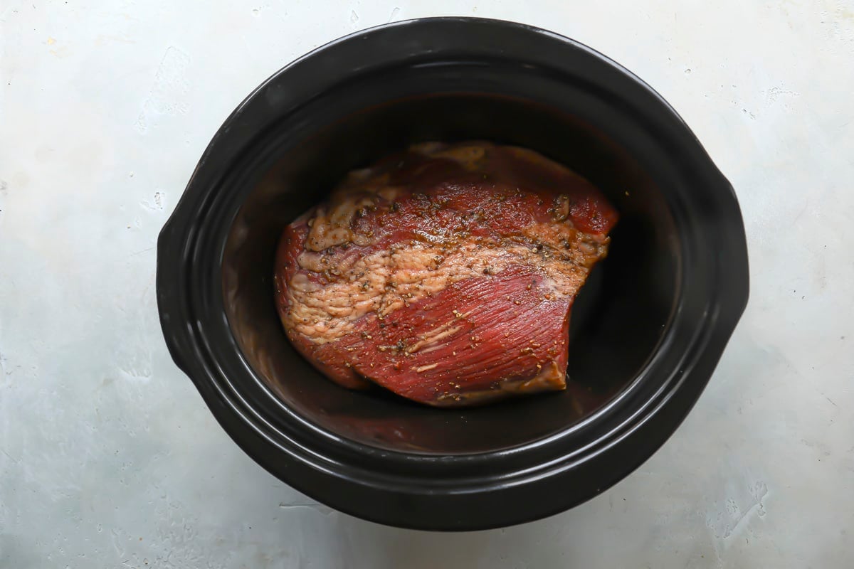 A seasoned beef brisket in a crockpot before being cooked.