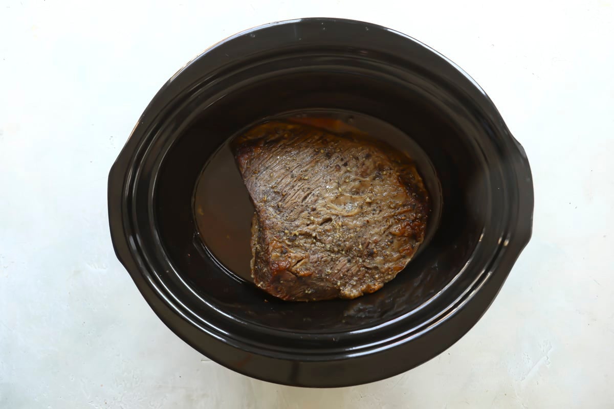 A cooked beef brisket in a slow cooker.