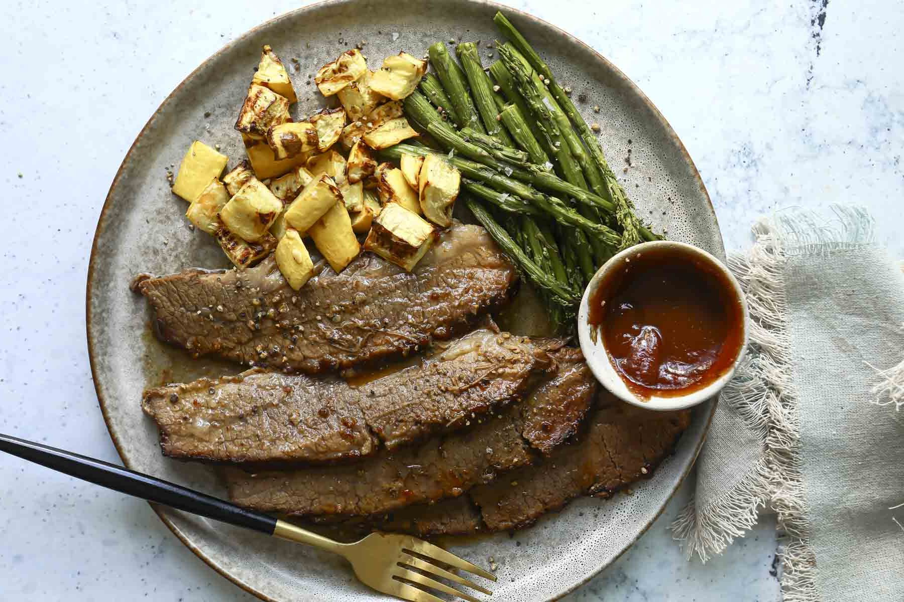 Slow cooker bbq beef brisket on a plate with potatoes and asparagus.
