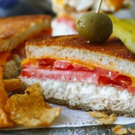 A halved tuna melt on parchment paper next to kettle chips.