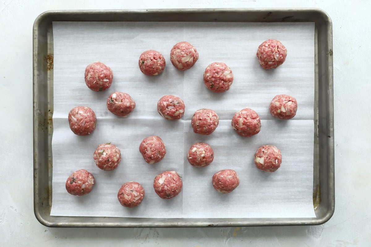 Raw meatballs on a parchment paper lined baking sheet.