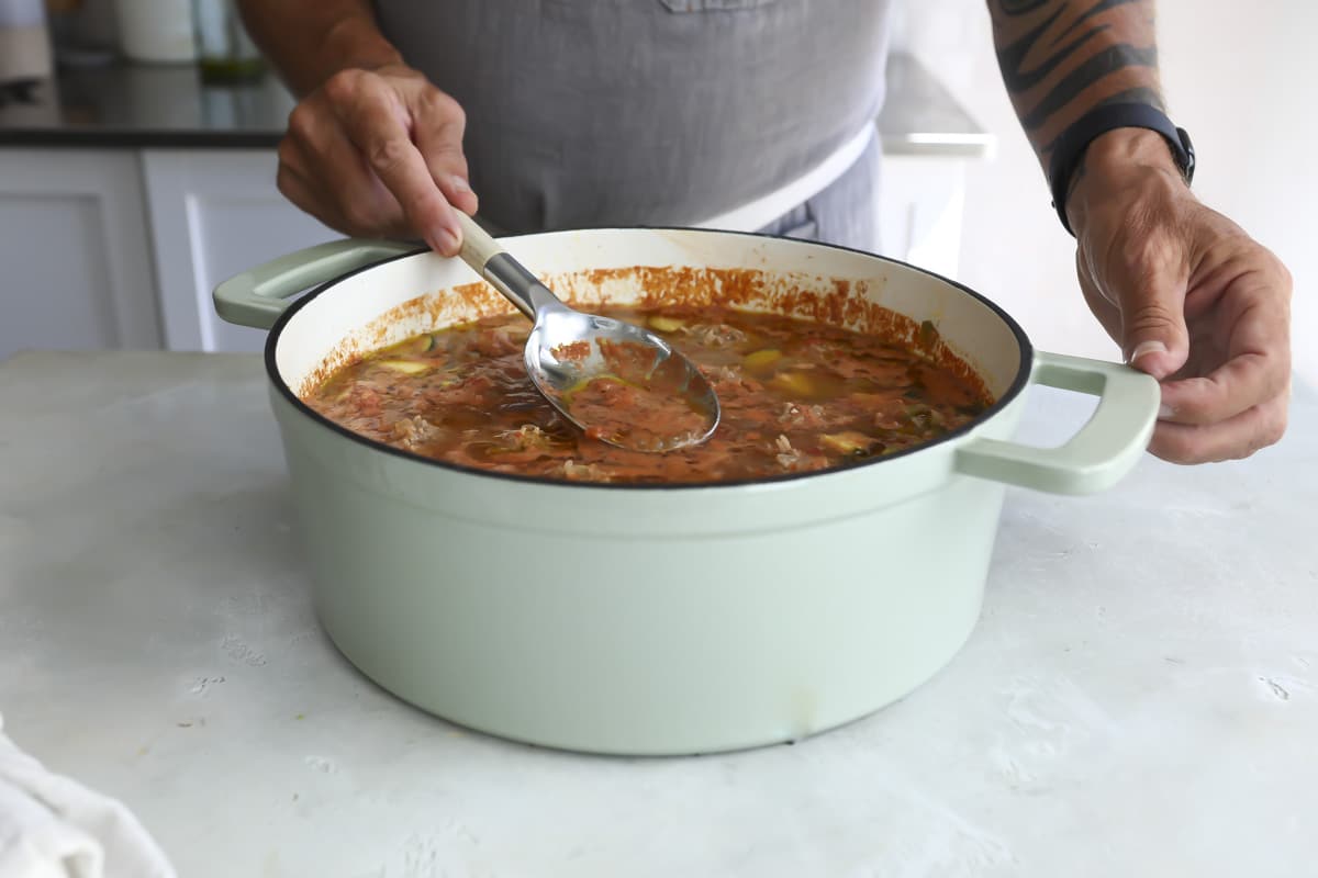 Someone skimming fat off of the top of Albondigas soup.