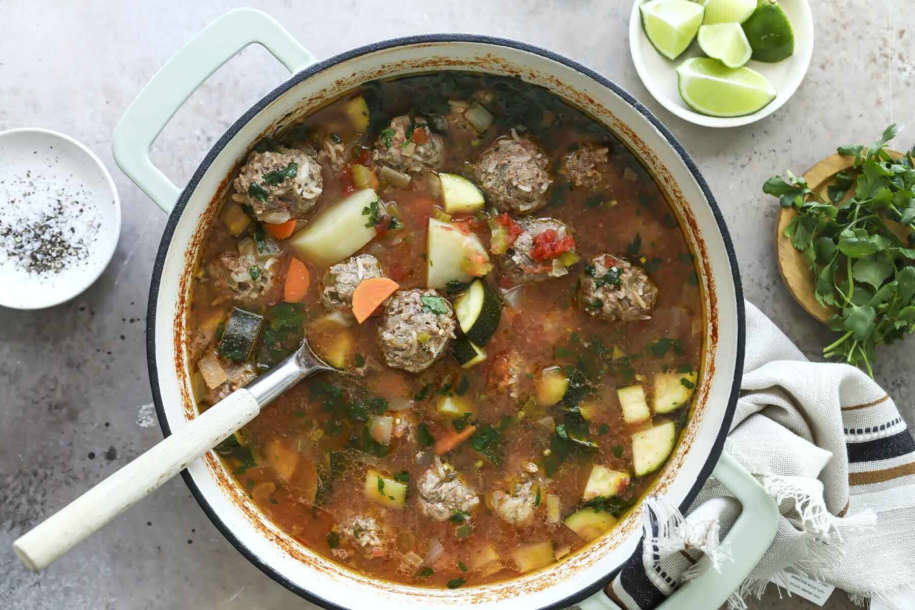 A pot of Albondigas soup with a spoon resting in it.