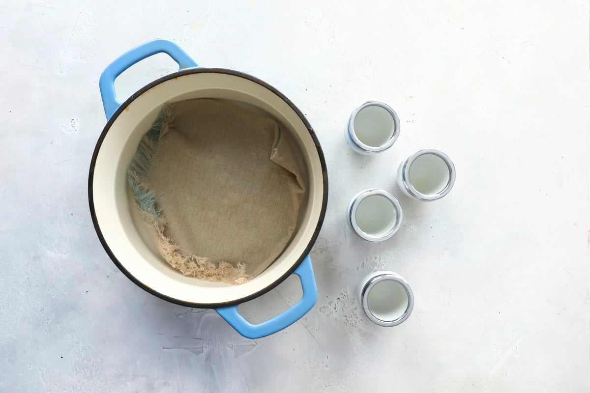 A pot with a towel on the bottom next to 4 egg coddlers.