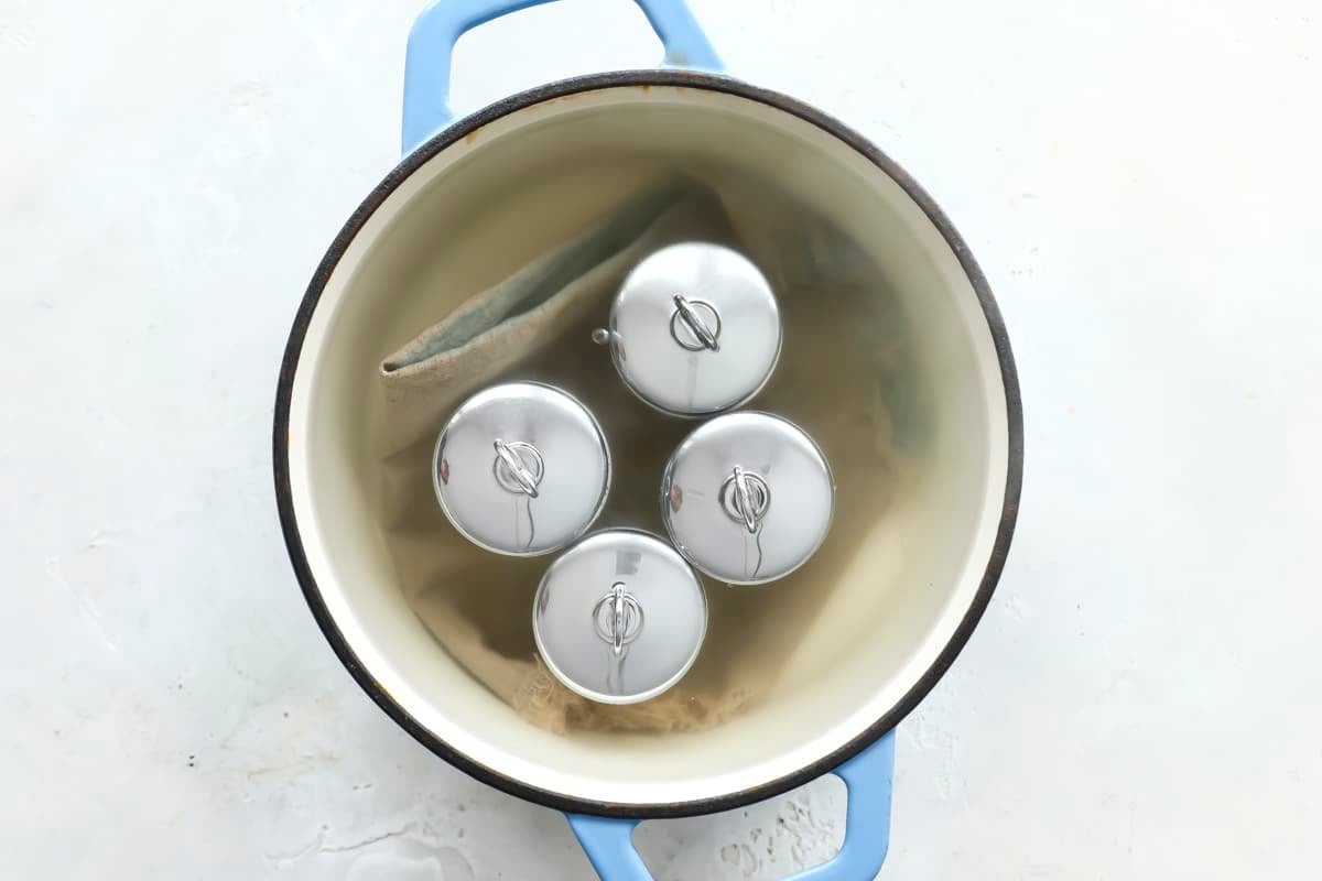A pot with a towel on the bottom and 4 egg coddlers inside.