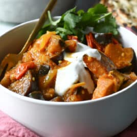 A bowl of eggplant curry with yogurt on top.