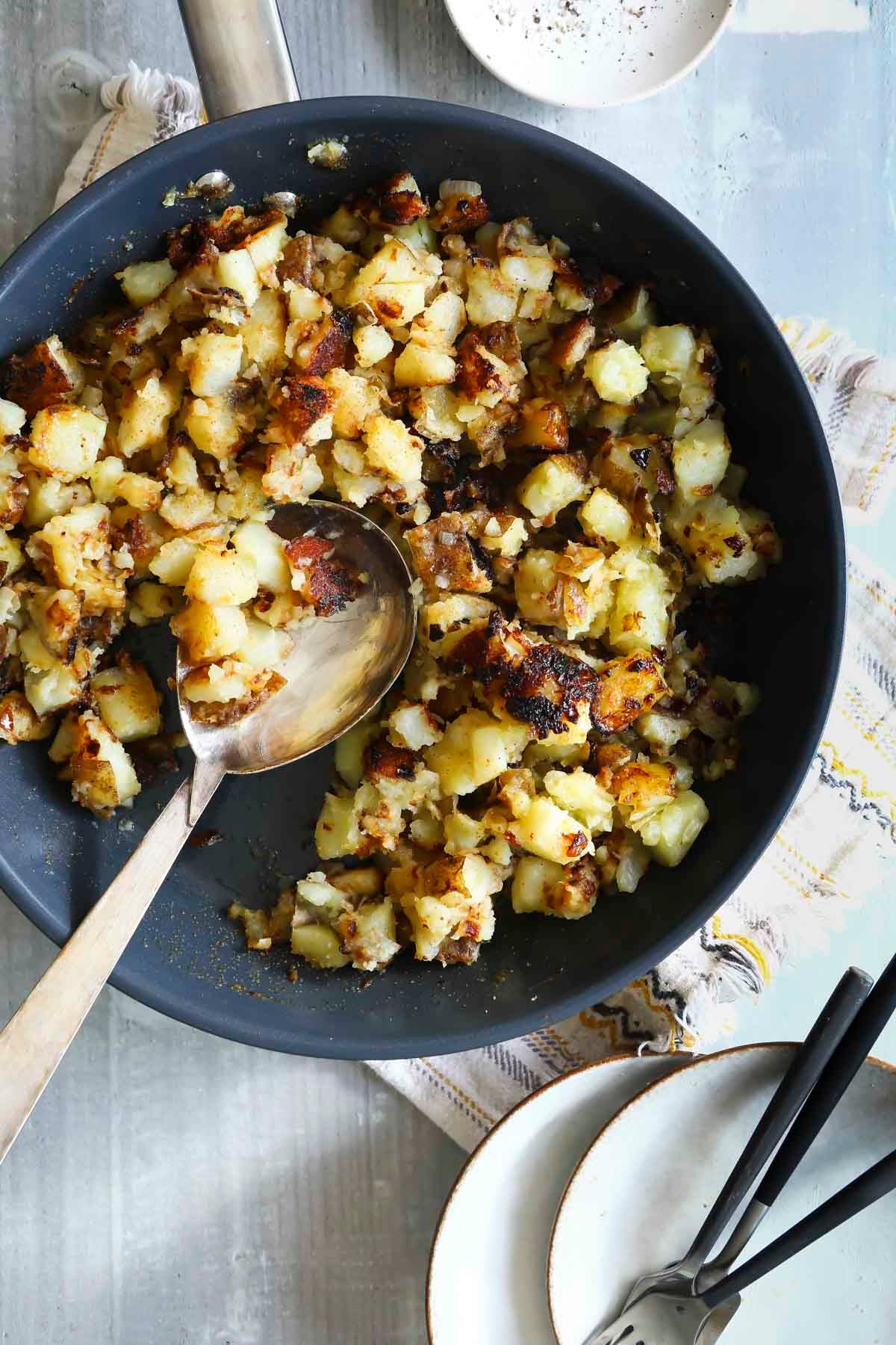 A skillet of home fries with a wooden spoon.