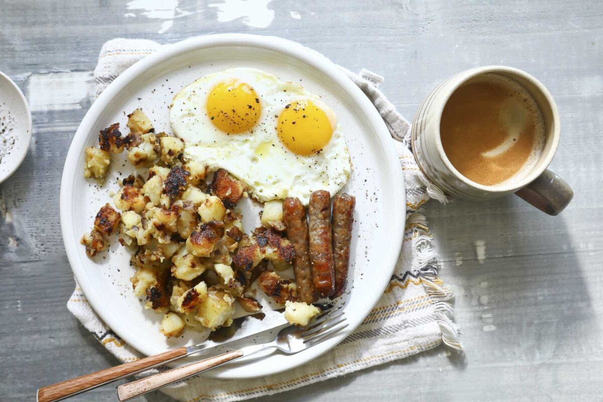 A plate of home fries with fried eggs and bacon.
