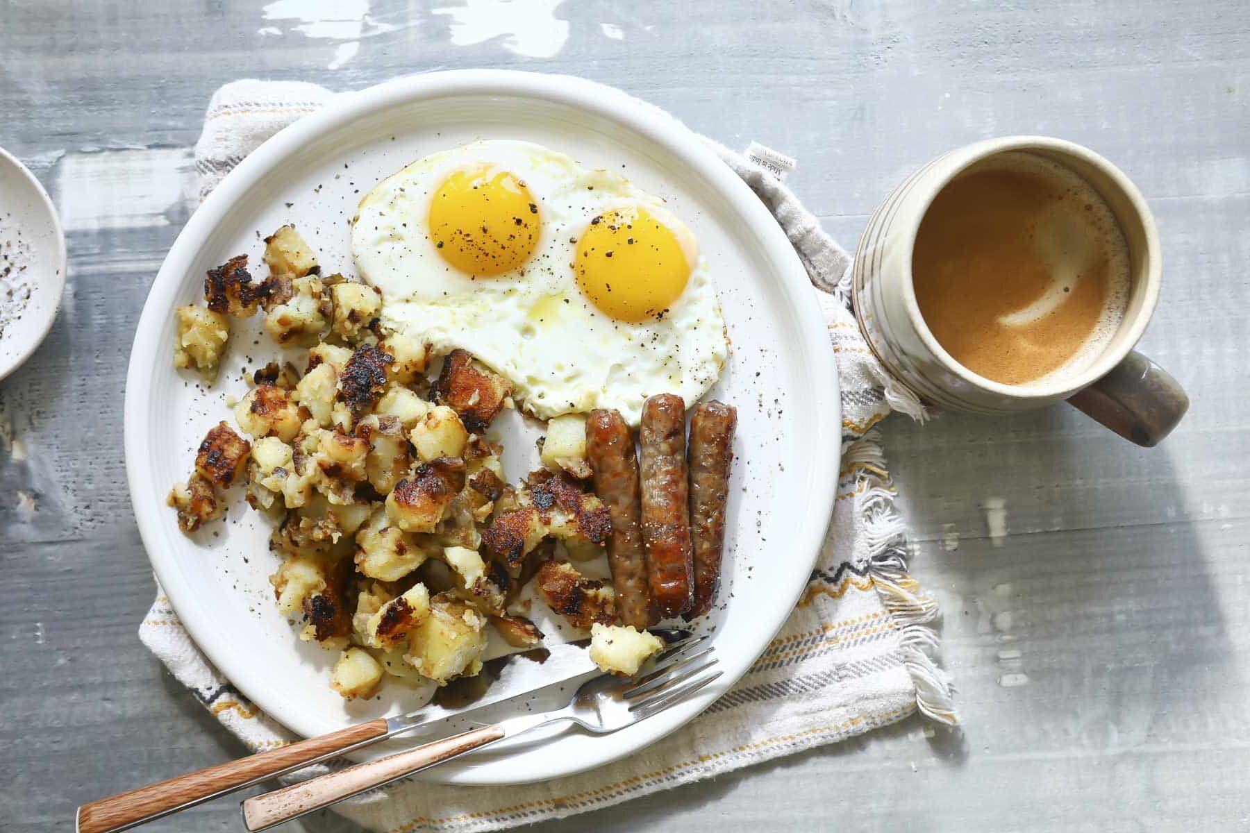 A plate of home fries with fried eggs and bacon.