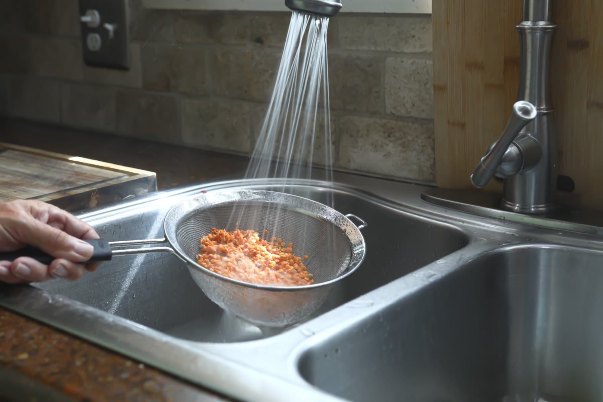 Rinsing dry red lentils in a strainer in the sink.