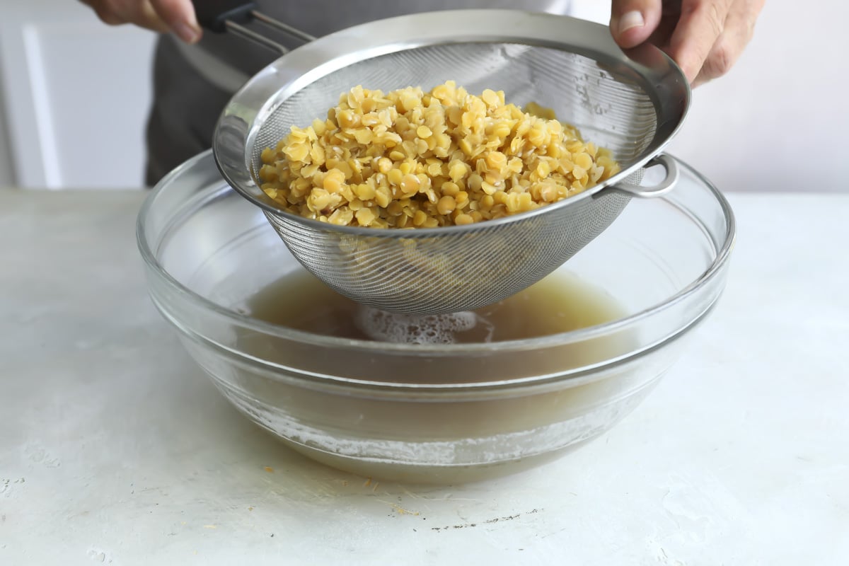Draining cooked red lentils in a strainer.