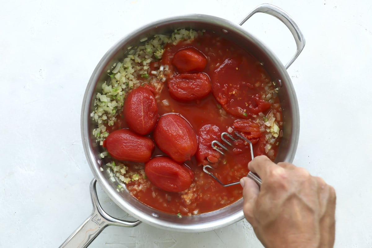Smashing tomatoes in a skillet with onions.
