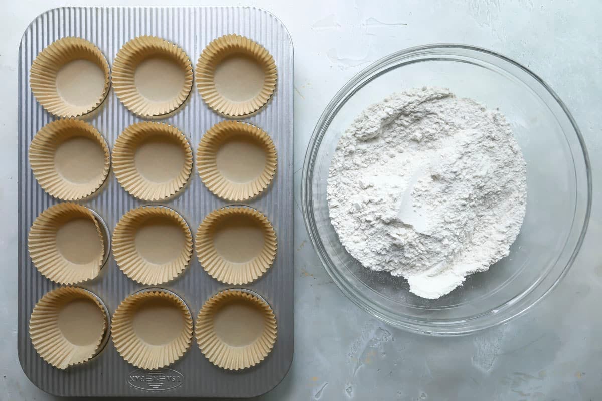 Dry ingredients for muffins next to a muffin tin lined with paper liners.