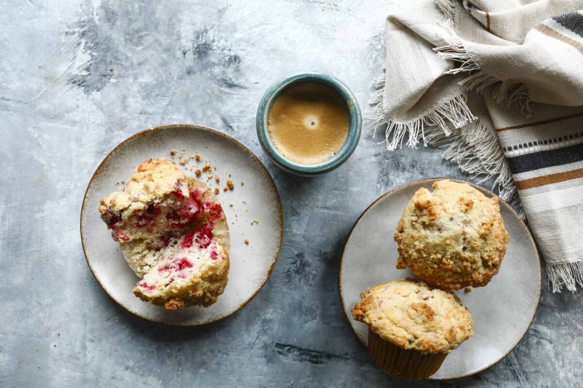 A raspberry muffin on a plate, split open, near a cup of coffee.