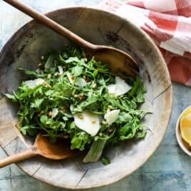 A bowl of arugula salad with pine nuts.