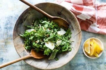 A bowl of arugula salad with pine nuts.
