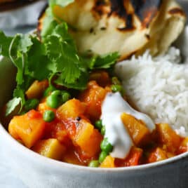 A bowl of potato curry with rice and naan on the side.