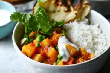 A bowl of potato curry with rice and naan on the side.