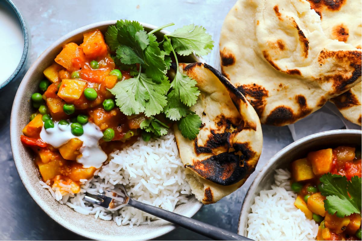 A bowl of potato curry with rice and naan on the side.