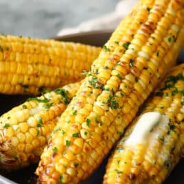A gray serving dish with four cooked cobs of corn in it.