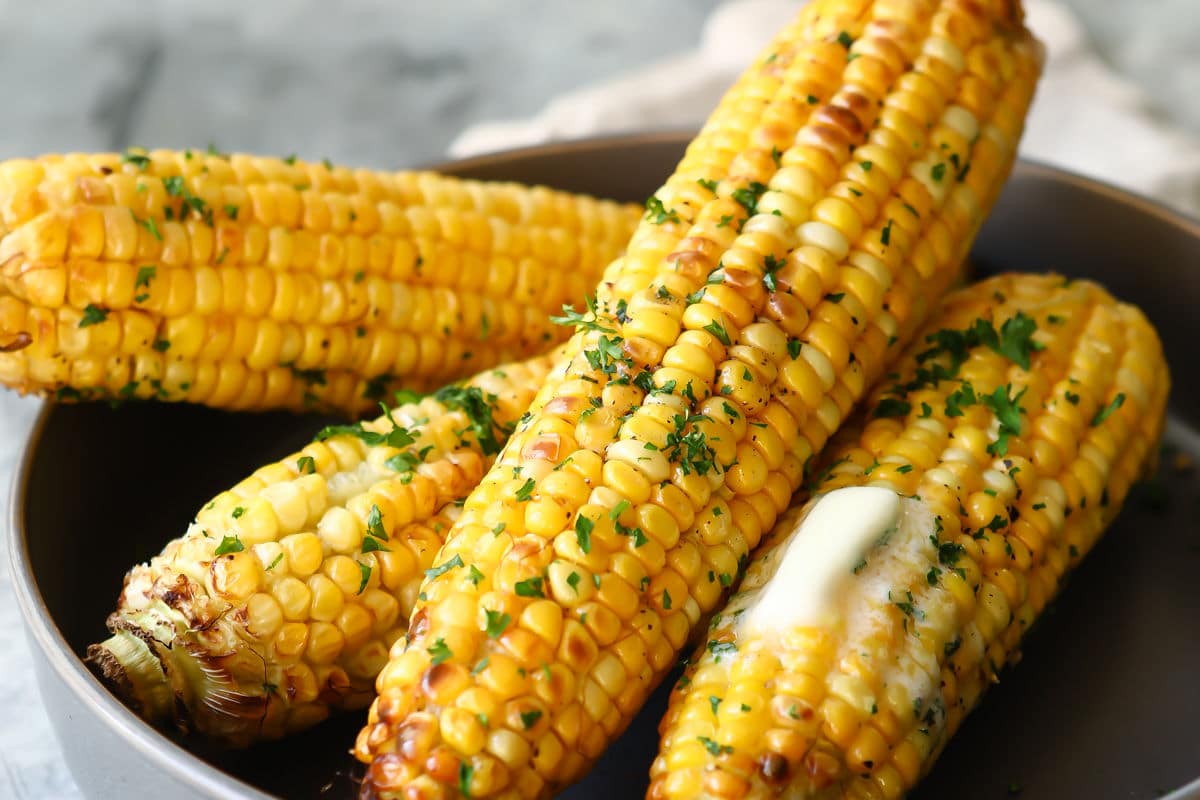 A gray serving dish with four cooked cobs of corn in it.