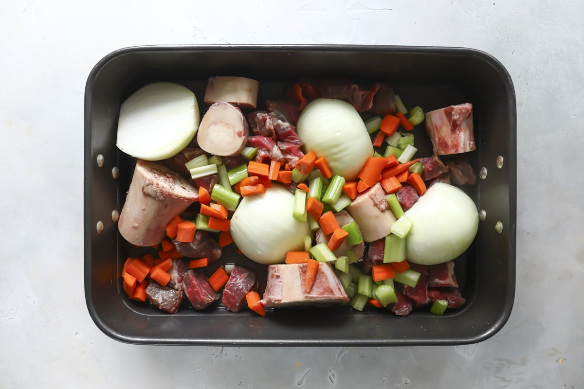 A pan of marrow bones, raw beef, and fresh vegetables.
